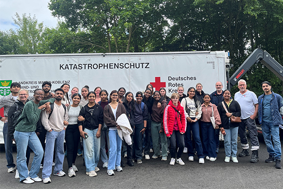 Große Gruppe mit Pflegeschüler:innen vor einem Katastrophenschutz-Container des DRK