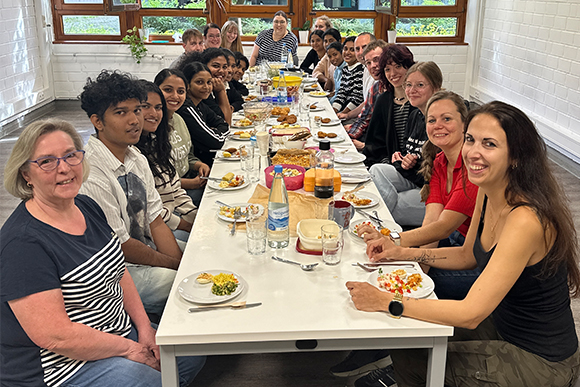 Menschen unterschiedlicher Kulturen sitzen gemeinsam an einer großen Tafel mit verschiedenen Speisen in der Mitte.